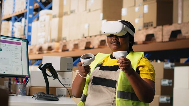 Black female employee with virtual reality glasses handling orders fulfillment via 3D simulation, parcel status on package tracking software. Artificial intelligence inventory control. Camera B.