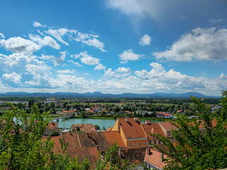 City panorama with orange rooftops, river and mountains under blue sky