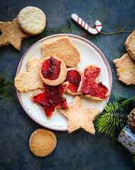 Christmas buttery biscuits with red fruit jelly on a white plate and a rustic gray background