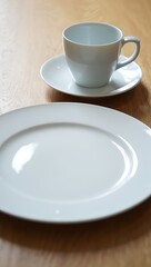 Fototapeta premium A Simple White Cup and Saucer Beside a Clean Plate on a Wooden Table