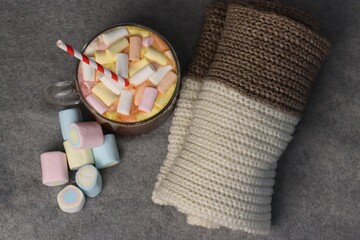 Delicious hot cocoa with marshmallows and red-and-white straw next to knitted plaid on gray background — warm and cozy photo for seasonal advertising, coffee shop menus, social media, greeting cards, 