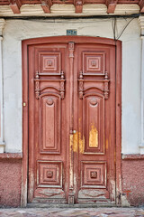 Ornate wooden double doors with intricate carvings and weathered paint, showcasing rich textures and historical charm, inviting exploration of the surrounding architecture in Cuenca Ecuador