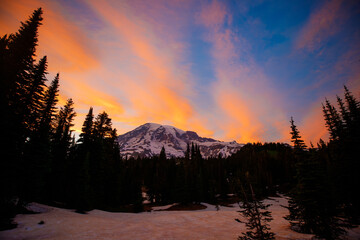 Stunning sunset over Mount Rainier, Washington. Vibrant sky with warm hues illuminating the rugged mountain peaks and surrounding forest.