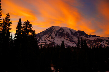Stunning sunset over Mount Rainier, Washington. Vibrant sky with warm hues illuminating the rugged mountain peaks and surrounding forest.