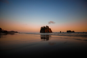 Wild coastal landscape at sunset on Second Beach, Olympic National Park, Washington. Driftwood on the shore, vibrant colors in the sky, and iconic sea stacks in silhouette.