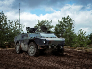 Fototapeta premium Military armored reconnaissance vehicle positioned in muddy terrain with natural vegetation cover