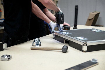 Worker hands using drill to assemble flight case hardware components in production workshop