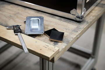 Workshop table displaying aluminum components calipers and wood samples for flight case manufacturing