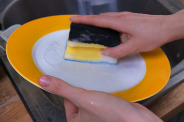 Washing Dishes Hands scrubbing a plate in a kitchen sink with soapy water