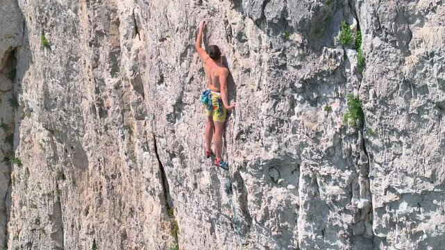 AERIAL, CLOSE UP: Focused climber climbs the climbing route in steep limestone wall in dynamic positions and with deliberate choice of next holds. Young man doing adrenaline sports on a hot summer day