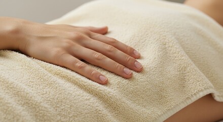 A hand rests on a creamcolored towel covering a persons torso The nails are unpolished