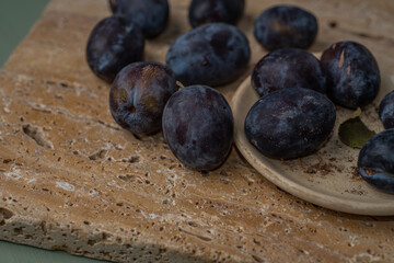Fresh ripe plums on stone surface with rustic plate, close up