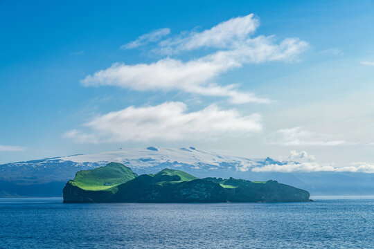 Snow capped mountains behind uninhabited island of Ellidaey Westman Islands in the South of Iceland