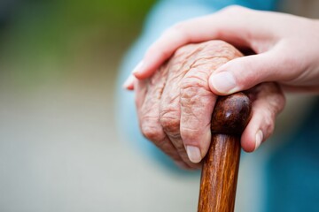 Wrinkled hand of a senior person holding a walking stick is receiving support from a younger person, conveying care and assistance