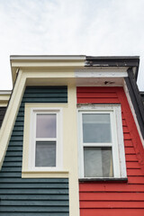 Two vintage houses adjoined, one is red and the other is green. There are multiple double-hung windows with white trim in the old houses. The hip roof has black shingles. There’s a dormer on the top.