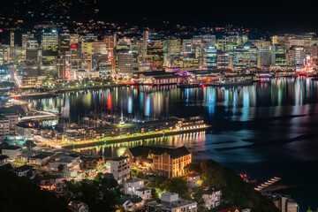 A view of Wellington, the capital city of New Zealand with the central city buildings illuminated at night and reflected in the harbour. The view is from an elevated position on Mount Victoria.