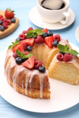 Pieces of delicious bundt cake with berries, glaze and mint on light blue wooden table, closeup