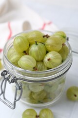 Fresh green gooseberries in jar on white table, closeup
