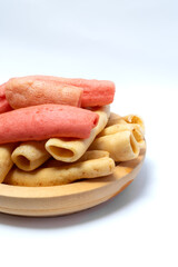 Traditional crackers in red and cream colors arranged on a wooden plate with white background, representing Asian snack culture, crispy food, and tasty appetizer.