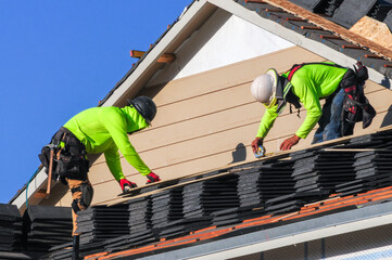 Roofers install rows of stacked shingles on a new house under construction, wearing safety gear and bright protective clothing as part of the residential building process © Eduardo Barraza