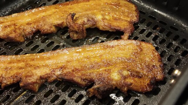 Close-up of pork ribs sizzling while cooking in an air fryer basket