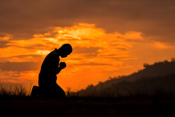 Christian prayer. Man on his knees praying on sunset background. Kneeling prayer to God. Worship and praise.