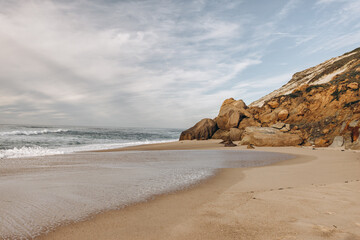 Portuguese coast. Foz de Arelho beach with orange-colored rocks on a cloudy day.