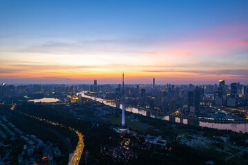 Naklejka premium Wuhan city skyline at dusk shows the river and bright lights illuminating the urban landscape.