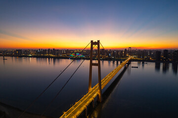 Fototapeta premium Wuhan china bridge crosses water under twilight sky and city lights glow.