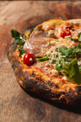 Close-up view of a pizza with vegetables and grated cheese on a wooden table.