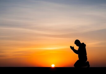 Obraz premium Silhouette of a man kneeling in prayer against a sunset