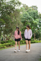 Obraz premium Two Young Women Wearing Athletic Wear Walking Together on a Scenic Pathway Surrounded by Lush Greenery in a Park Environment
