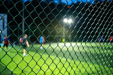 People playing soccer behind a metal chain link fence at night