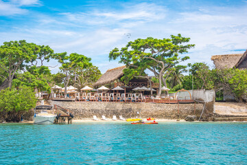 Serene beach view showcasing a coastal restaurant, lush trees, and clear turquoise waters at Rosario Islands, Cartagena, Colombia.