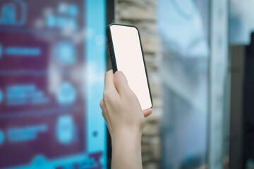 A Hand Holding a Smartphone with Blank Screen in Front of Digital Display