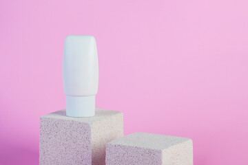 Plastic white tube for cream or lotion. Skin care or sunscreen cosmetic with stylish props on pink...