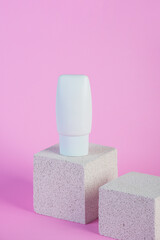 Plastic white tube for cream or lotion. Skin care or sunscreen cosmetic with stylish props on pink background.