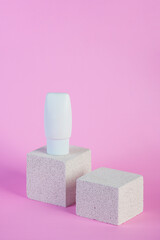 Plastic white tube for cream or lotion. Skin care or sunscreen cosmetic with stylish props on pink background.