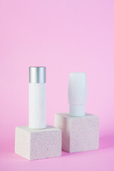 Plastic white tube for cream or lotion. Skin care or sunscreen cosmetic with stylish props on pink background.