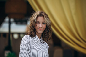A teenage girl model is young and beautiful in a shirt and trousers on the street in a street cafe