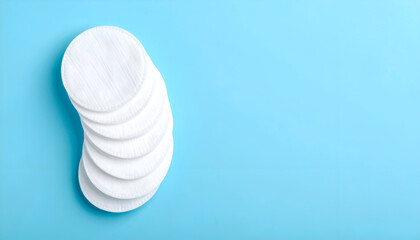 Pristine stack of soft white cotton pads, neatly arranged on a serene light blue background, offering generous negative space. Ideal for beauty, health, and cosmetic design concepts