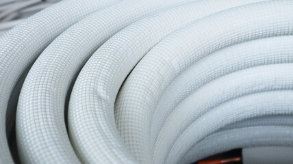A close-up of a coiled white air conditioning refrigerant pipe, showing its textured, insulated...
