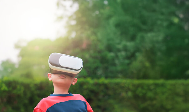 Young boy wearing virtual reality headset outdoors, child experiencing VR technology in nature, kid playing immersive digital game with modern gadget. Virtual reality while sitting outdoors.