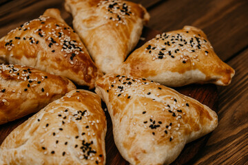 platter holds six golden-brown samsa, freshly baked and sprinkled with black and white sesame seeds. crispy crust invites attention. close up.