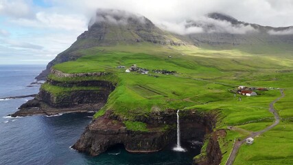 Aerial view of Gásadalur waterfall plunging into the Atlantic Ocean, framed by dramatic cliffs, lush green Faroe Islands landscape, and traditional village houses