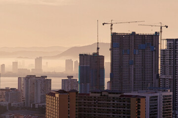 View of a city and a bridge at sunset. A high-angle view of a city with buildings and the Penang bridge in the background during a beautiful orange-toned sunset.
