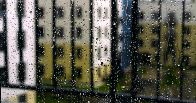 Close view of raindrops clinging to window glass with out of focus colorful facades of residential high rise buildings in rainy cloudy day atmosphere