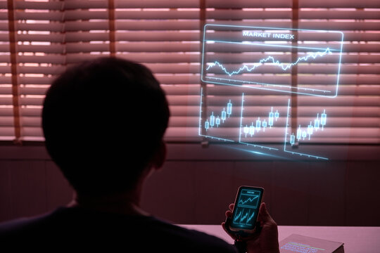 Man analyzing stock market data on a futuristic holographic display projected from a smartphone in a dark office. - Powered by Adobe