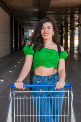 Smiling woman with shopping cart outdoors in supermarket area