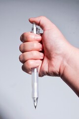 Hand pressing on mechanical pencil to refill or push graphite lead isolated on vertical background.